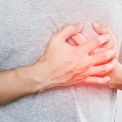 Dłoń na piersi, czerwony obszar sugeruje ból lub nierówne bicie serca.