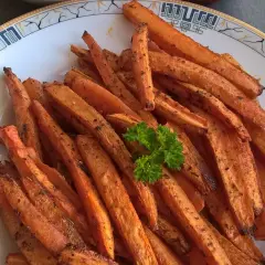 Chrupiące, pieczone frytki z marchewki, doprawione ziołami, podane na talerzu z natką pietruszki.