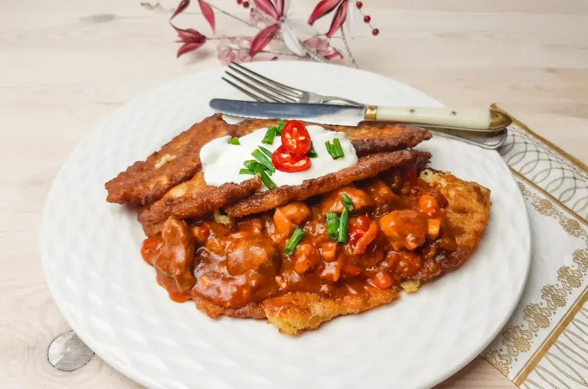 Pyszny placek po węgiersku z gulaszem, śmietaną i szczypiorkiem, ozdobiony papryczką chili.